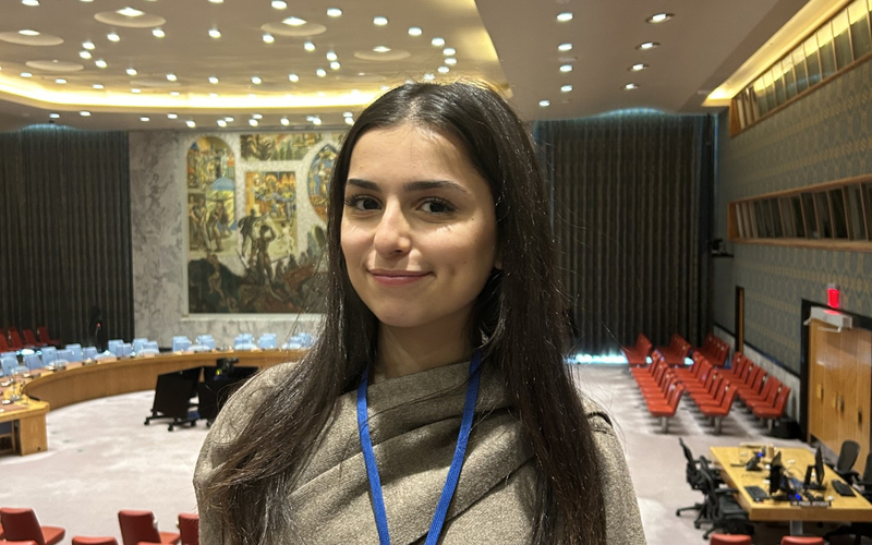 A girl standing in a large conference room with rows of red seats and a mural in the background.