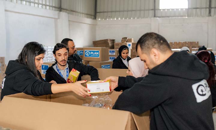 A man hands over a small box to a woman while they stand around a bigger box containing aid packages to be sent to people affected by the conflict in Gaza.  