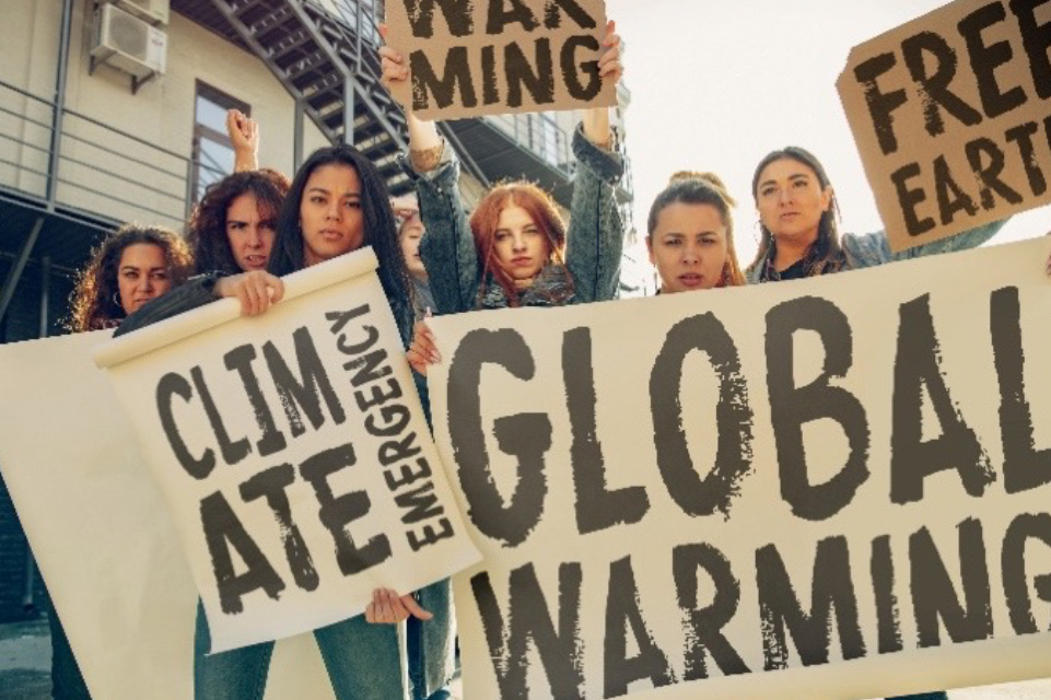 Young women with posters and signs reading “Climate emergency” and “Global warming” protest climate change on a street.