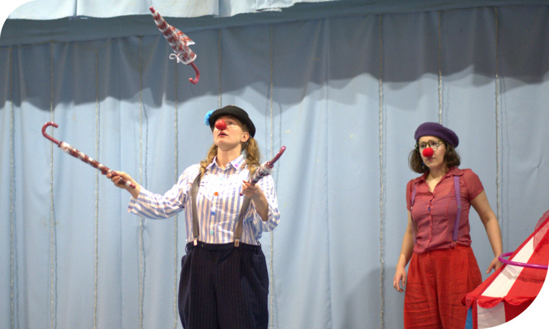 A person dressed as a clown juggles on a stage.