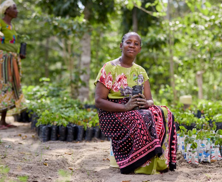 Caroline sits in the centre of the picture, holding a small plastic bag that contains a seedling.