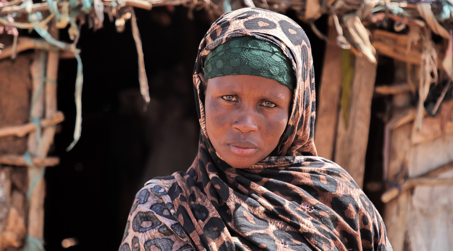 A woman standing in front of a makeshift home looking directly at the camera