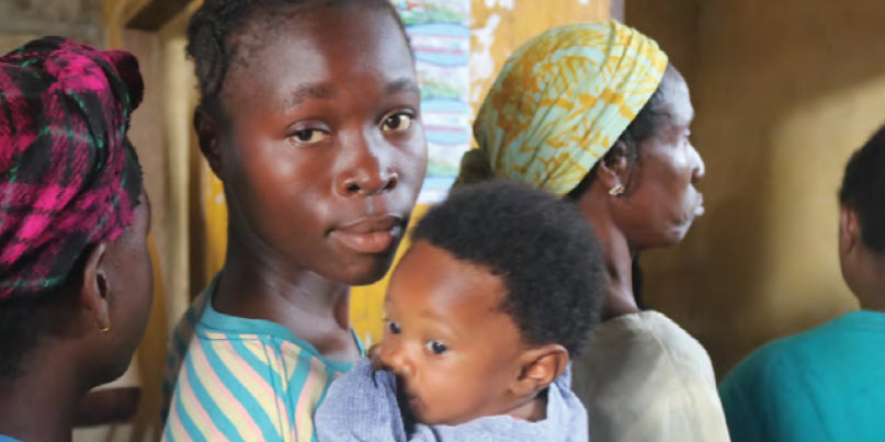 A mother in Liberia holding her young child waits in line to receive an insecticide‑treated mosquito net, which will protect her child from malaria. Plan distributed 6 million mosquito nets across Guinea, Liberia, and Senegal last year as part of our partnership with the Global Fund to Fight AIDS, Tuberculosis and Malaria.