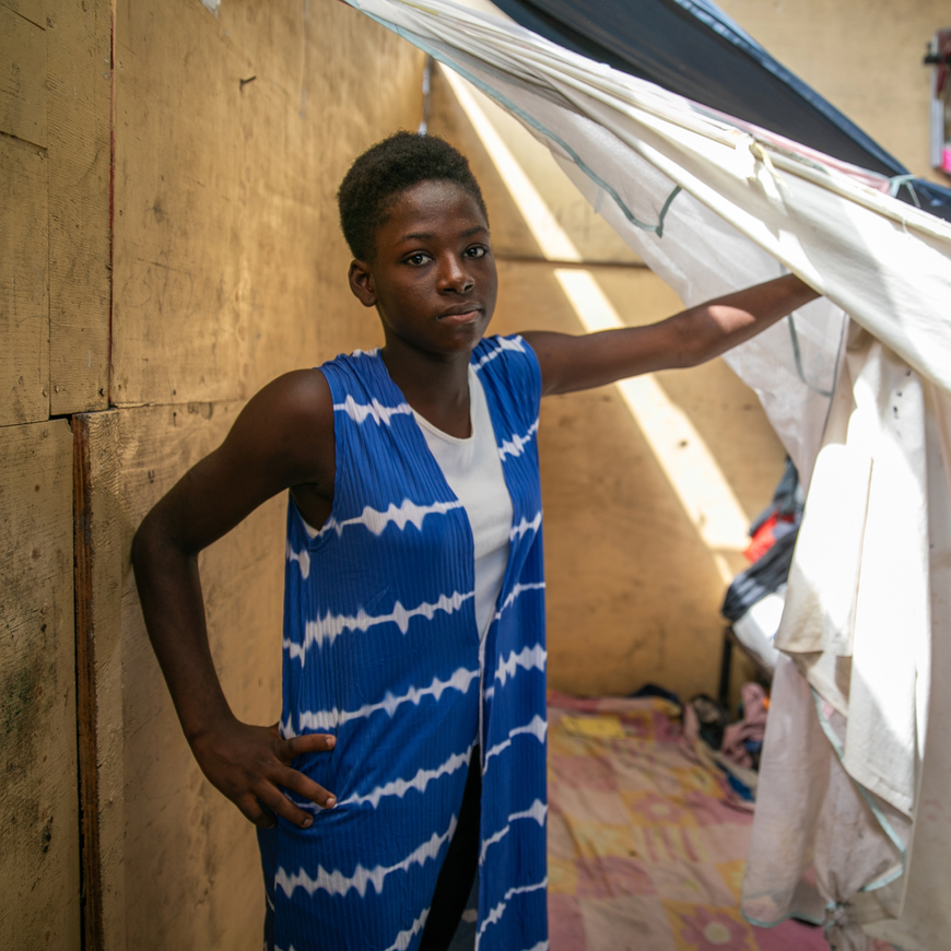 A girl standing in front of clothes hanging from the ceiling.