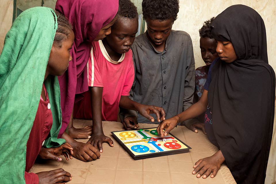 A group of children stand around a table playing a board game. 