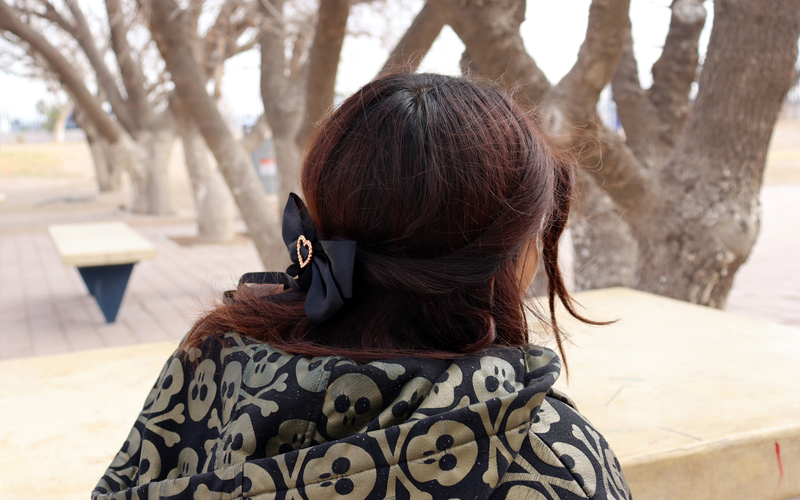 A girl with burgundy hair wearing a black bow looking away from camera.