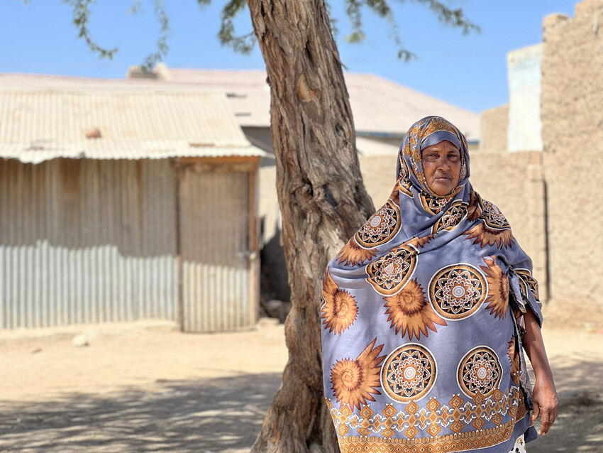 Ruqiya stands beside a tree in a sunny Somali yard. 