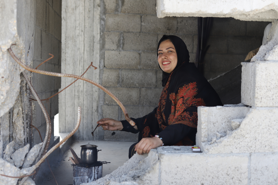 A woman smiles as she cooks in a building partially destroyed by airstrikes in Gaza.