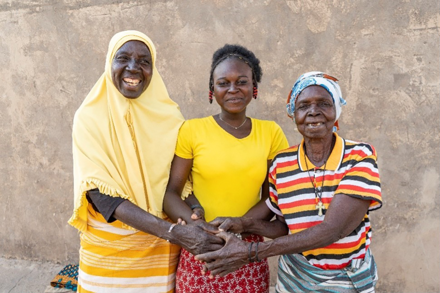 Two women and one teen girl wearing bright yellow clothing holding hands and smiling.