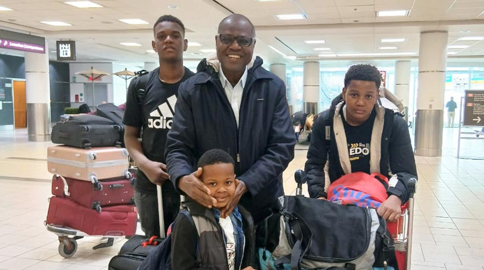 A man and three boys stand together in an airport with trolleys piled with suitcases.