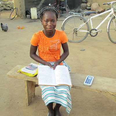 A girl sits smiling with a workbook and other school supplies