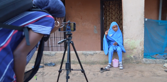 A woman looking into a phone set on a tripod and pointed at a girl using sign language.