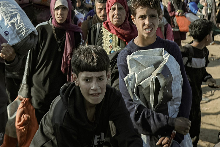 Children and families walk through a crowded area carrying their belongings.  Campaign to raise donations for GAZA EMERGENCY APPEAL.