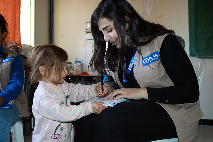 Farah'a daughter Aseel, 2, shows her drawing skills to Plan staff member 