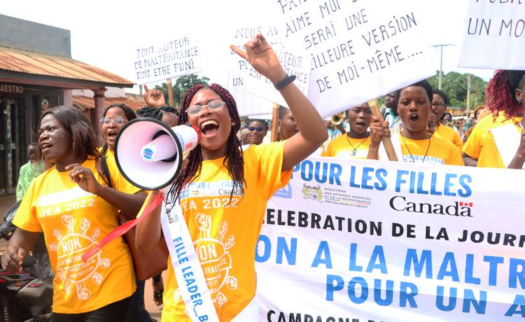 Girls march together in Benin, calling for an end to violence. One girl holds a megaphone, and others carry protest signs in the background.