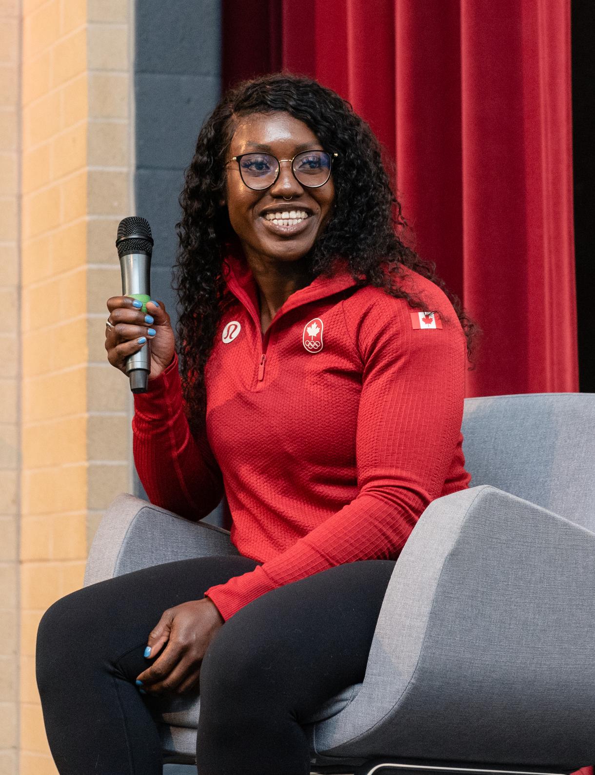 A woman wearing glasses sitting on stage holding a microphone during a panel discussion