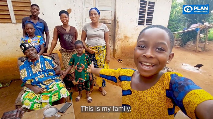 A screenshot from a video that shows a girl filming herself and her family of six in front of their home in Benin.