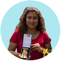 Sandra stands in a garden in Ecuador and shows off the medal she won for public speaking.