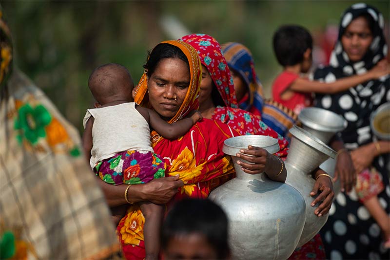 Bangladeshi woman carrying water and a child