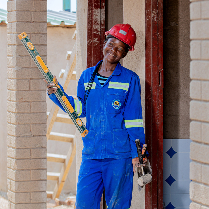 A young woman in a blue construction outfit holds tools while building outside.