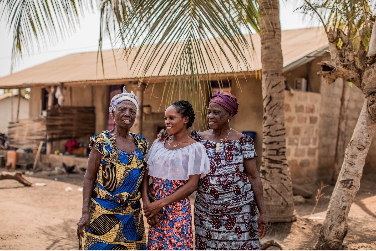 Two women and one girl standing outside wearing colourful clothing and smiling at each other