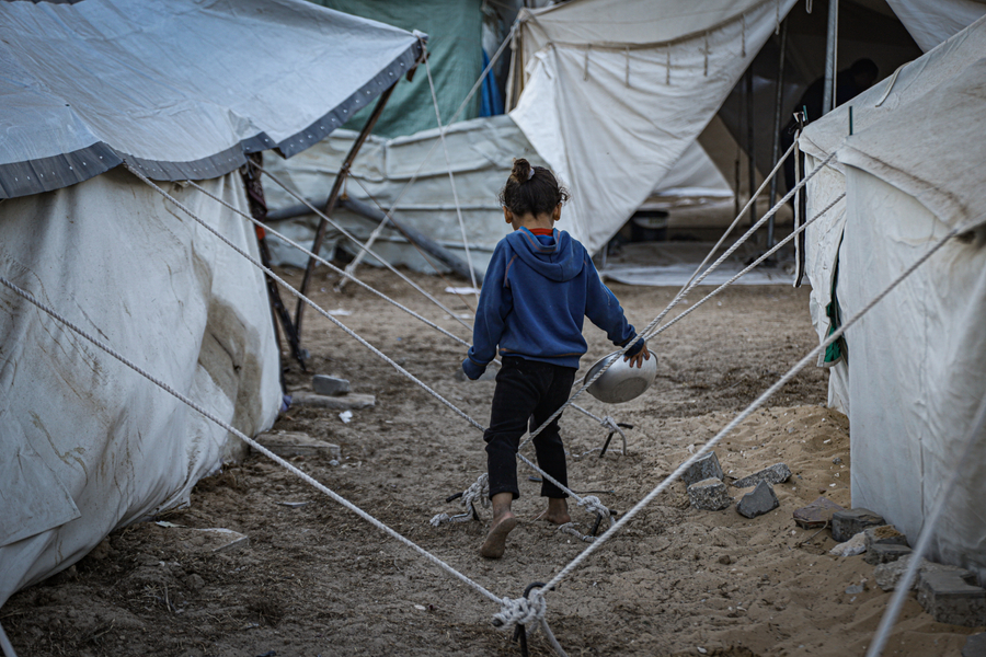 A child carries an empty plate for food at a displacement camp in Gaza.