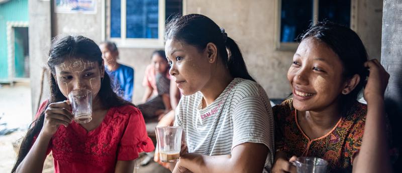 three young women sit at a table for food and drinks