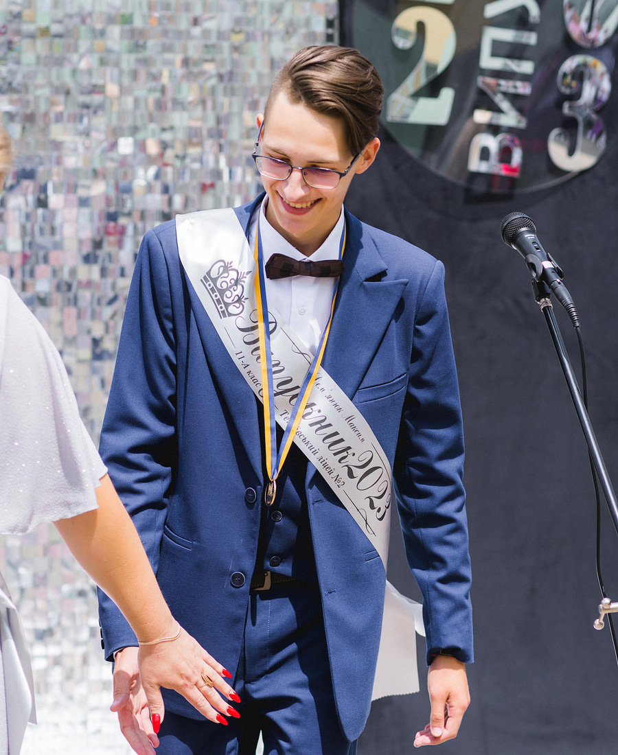 a young man wearing a graduation sash and smiling