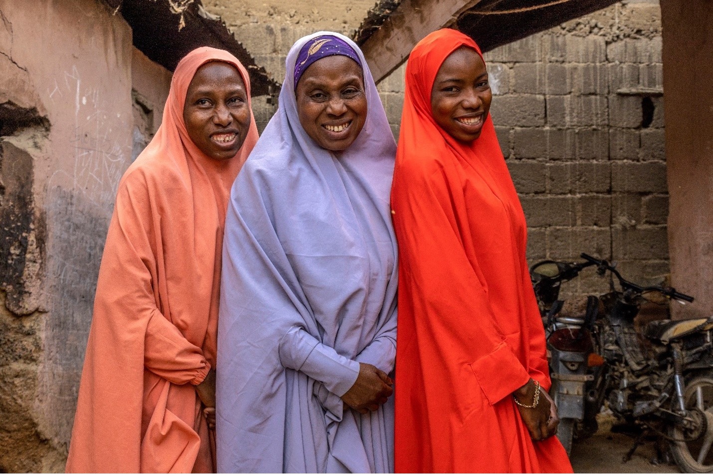 Two women and one girl standing outside wearing colourful clothing and smiling at each other