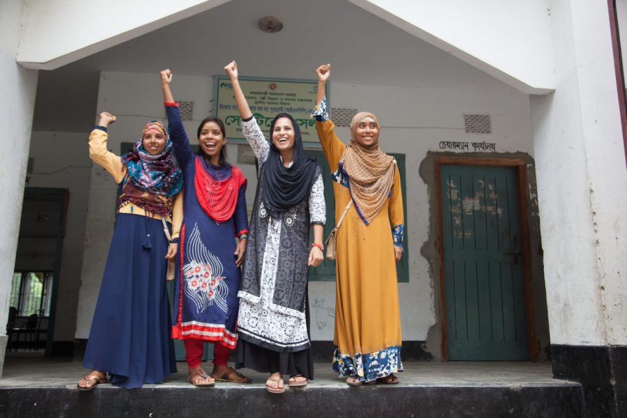 Four girls from Bangladesh cheer with arms raised in front of their school