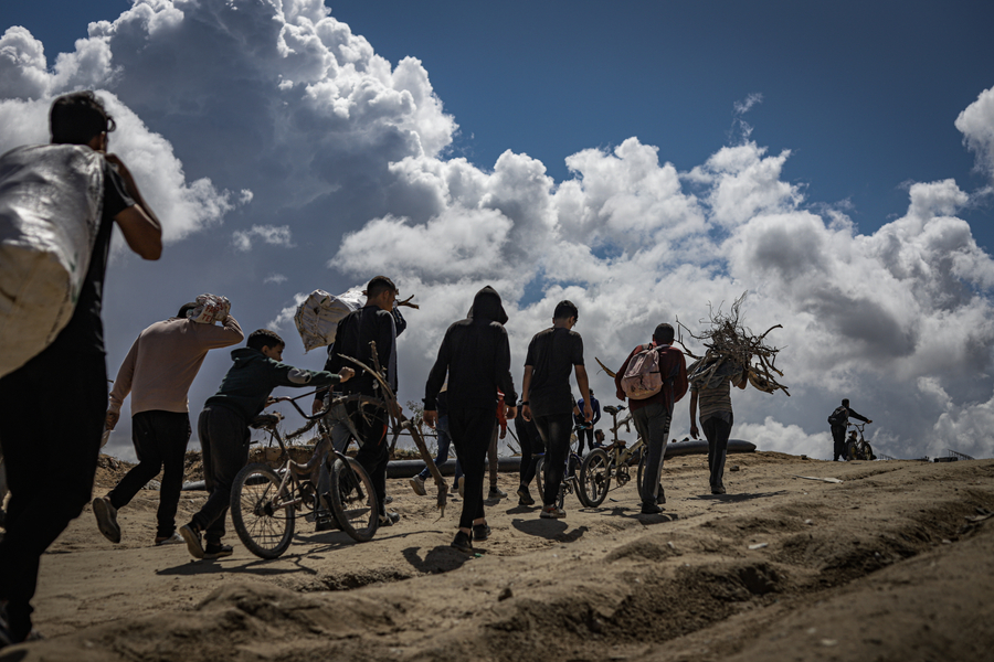 A group of men walk home after an aerial aid drop is canceled. Some carry firewood; a child wheels a bicycle alongside them.