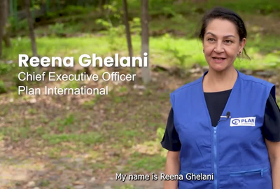 A woman in a blue Plan International-branded vest talking to camera.