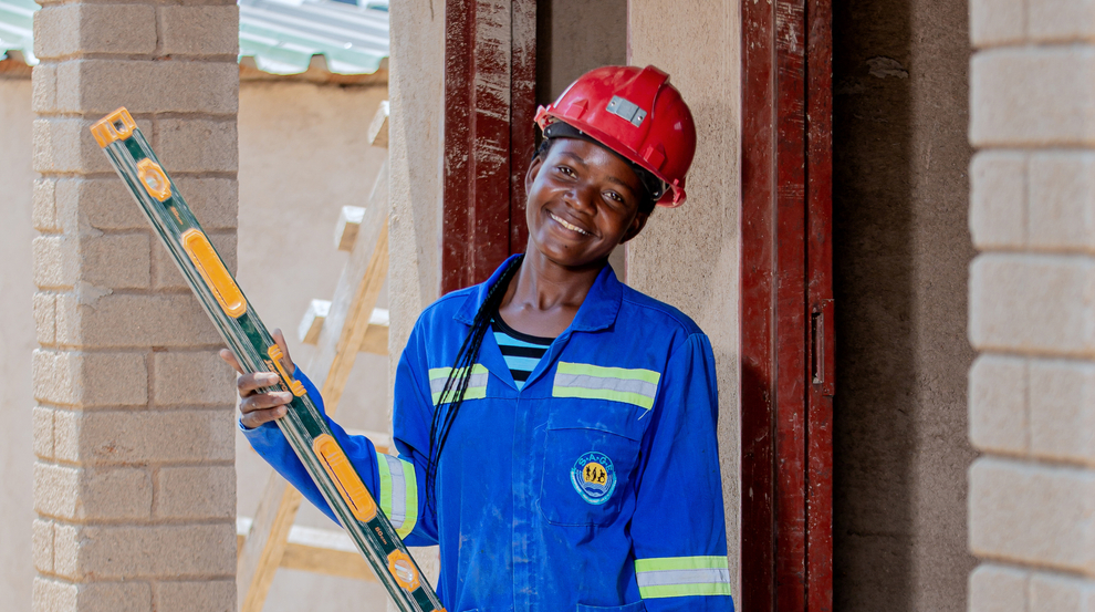 A young woman in a blue construction outfit holds tools while building outside.