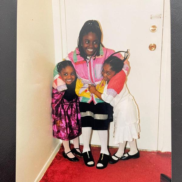 Three young girls who are dressed up and smiling and hugging each other in front of the door