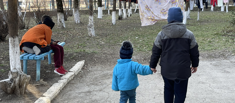 Two boys wearing winter clothes holding hands outside in a park.