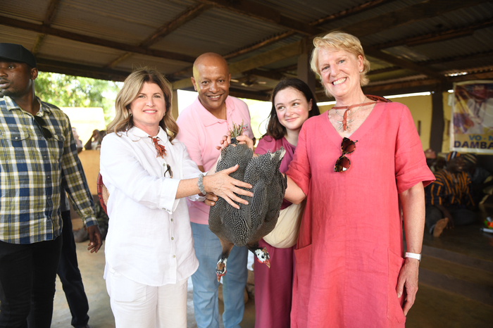 A woman with blonde hair holds onto a chicken while a man, a girl and a woman with short blonde hair smiles at the camera. 