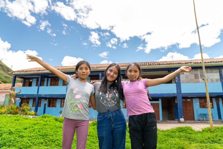 Three girls holding hands in front of school building in Peru