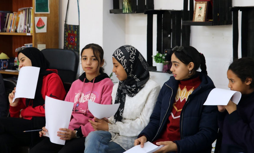 Girls sit side by side with papers in their hands in an office.