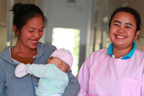 Two women laughing whilst holding a baby