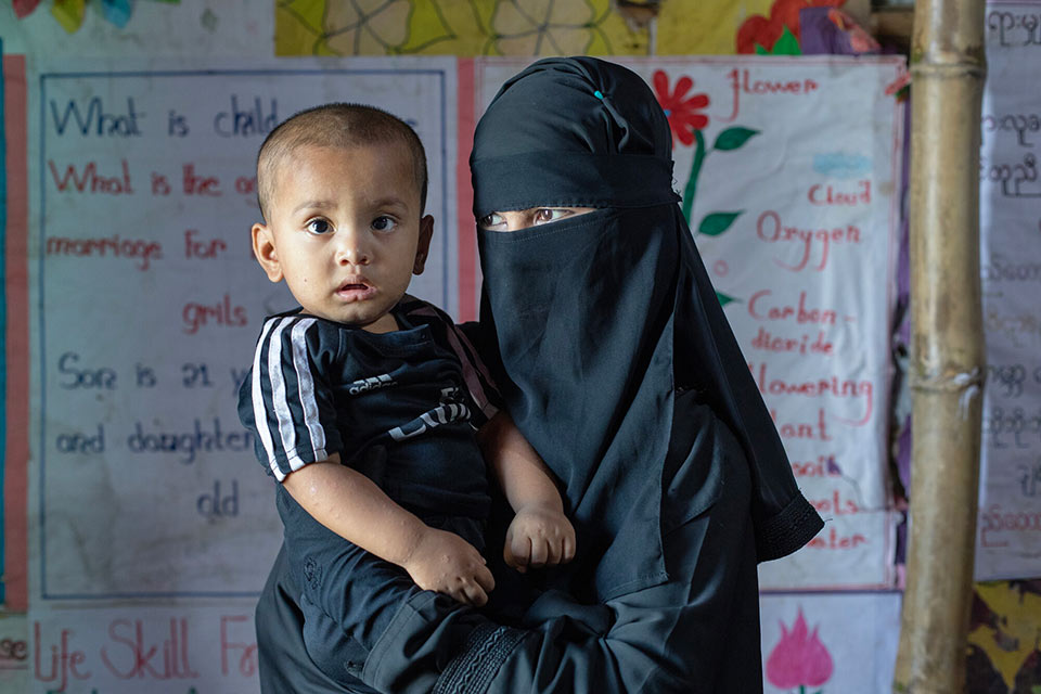 A woman in a black burqa holding a baby in a classroom.