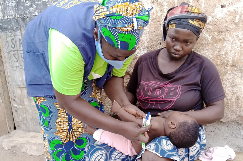 A mother holds her baby in her lap as a community health worker administers medicine to the child.