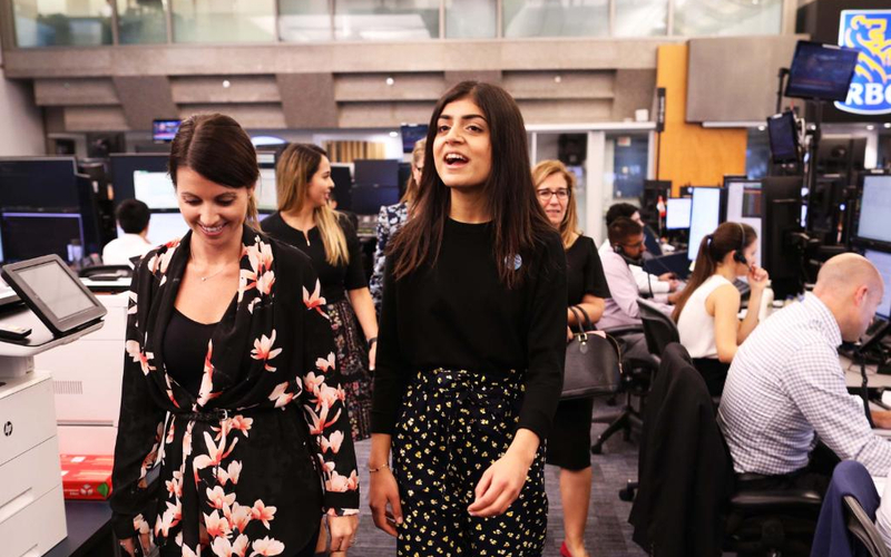 Two young women walk through a busy office workspace during a Girls Belong Here placement. 