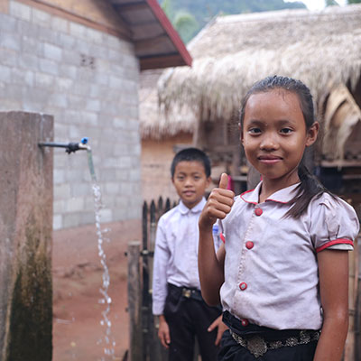 A girl gives a thumbs up beside a new Plan International water access point