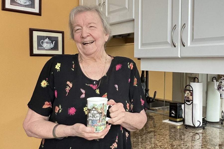 A woman holding a mug and smiling in her kitchen.