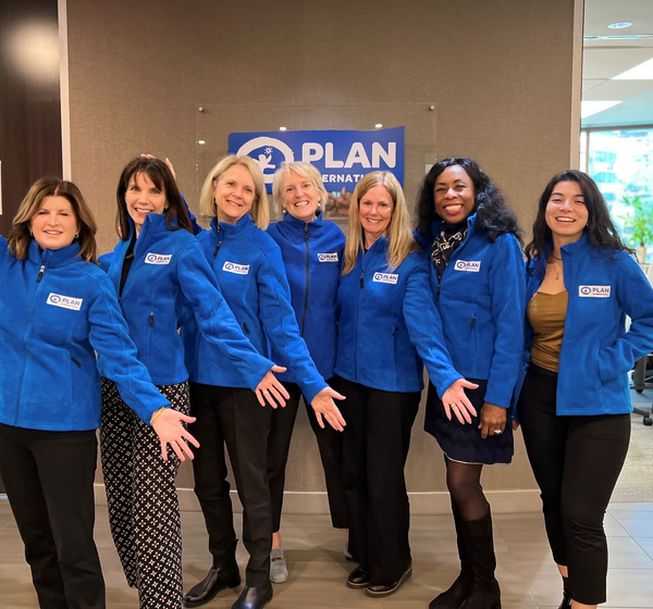 Seven women wearing matching Plan blue sweaters pose for a photo at the Plan office.