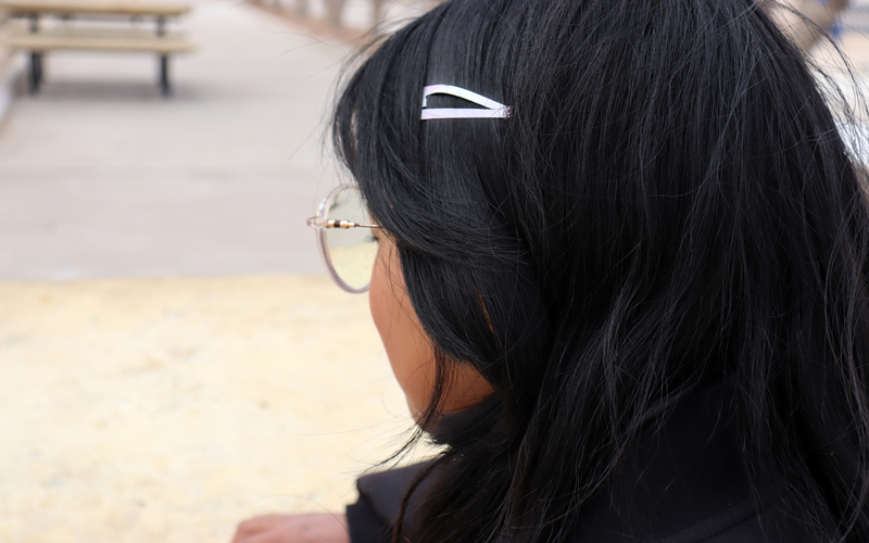 A girl wearing glasses and a white clip in her hair facing away from the camera.
