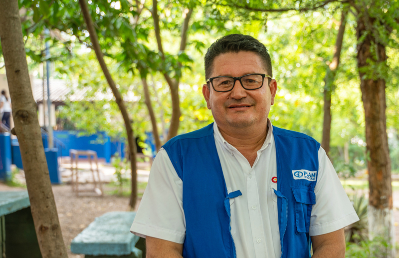  A man wearing a white shirt and a blue vest with the Plan International logo.