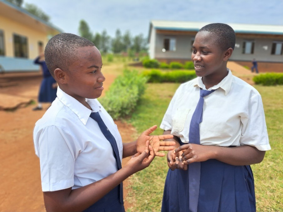 Two young girls in school uniforms standing and talking to each other outside in front of their school.