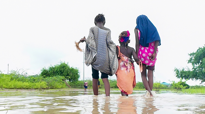 A group of three young women walking through muddy waters.
