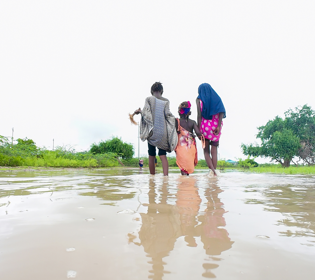 A photo of three children walking through muddy water after floods in Tana River County in Kenya.